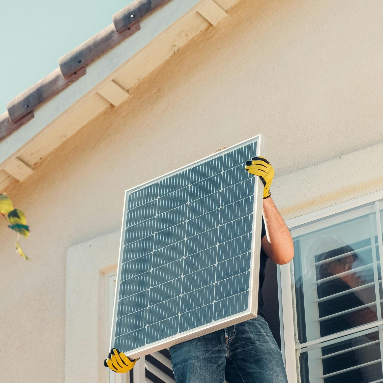Technician carrying a solar panel on a rooftop for installation, promoting renewable energy.